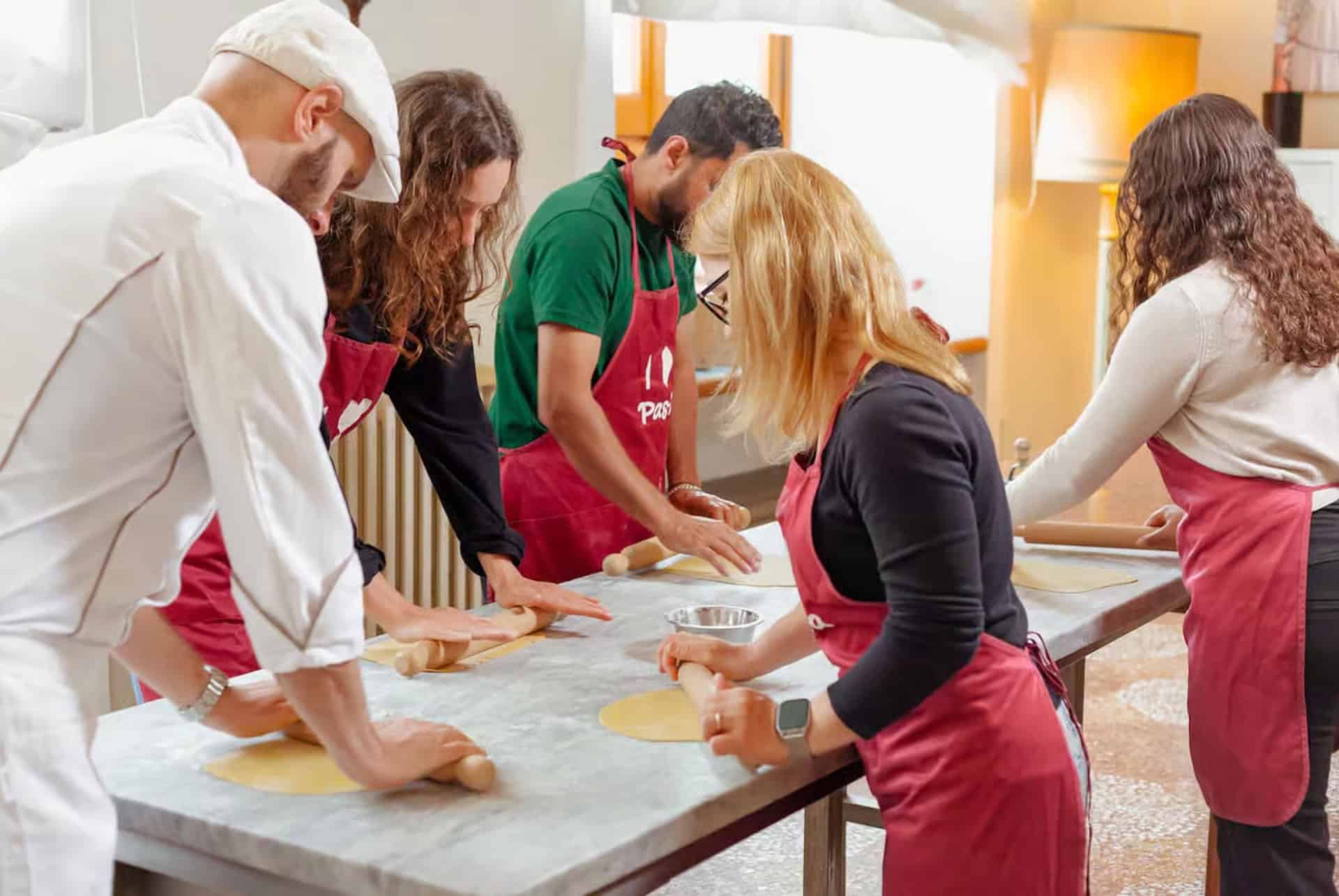 Participants en tablier étalant de la pâte fraîche au rouleau avec un chef, lors d’un atelier de pâtes à Venise Participants en tablier étalant de la pâte fraîche au rouleau avec un chef, lors d’un atelier de pâtes à Venise